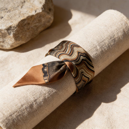 Bracelet large en twill de soie horizons boutique, motif abstrait effet tronc d'arbre, couleurs beige et brun, noué sur un rouleau de tissu.