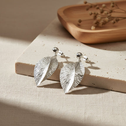 Boucles d'oreilles pendantes argentées en forme de feuilles croisées, finition martelée à la main, par Horizons Boutique.