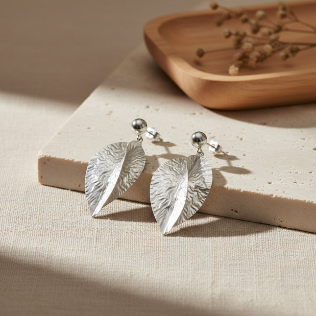 Boucles d'oreilles pendantes argentées en forme de feuilles croisées, finition martelée à la main, par Horizons Boutique.