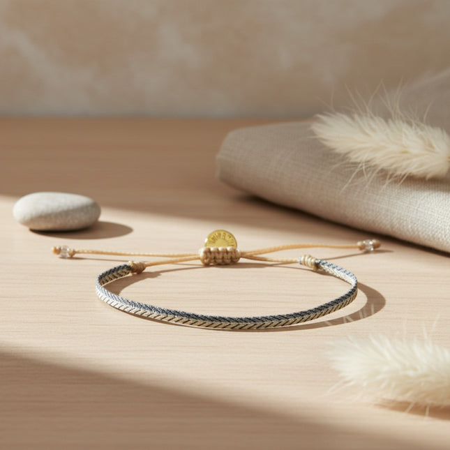 Bracelet fin tissé main horizons boutique en tons argent, 3mm de large, avec cordon ajustable et breloque dorée.