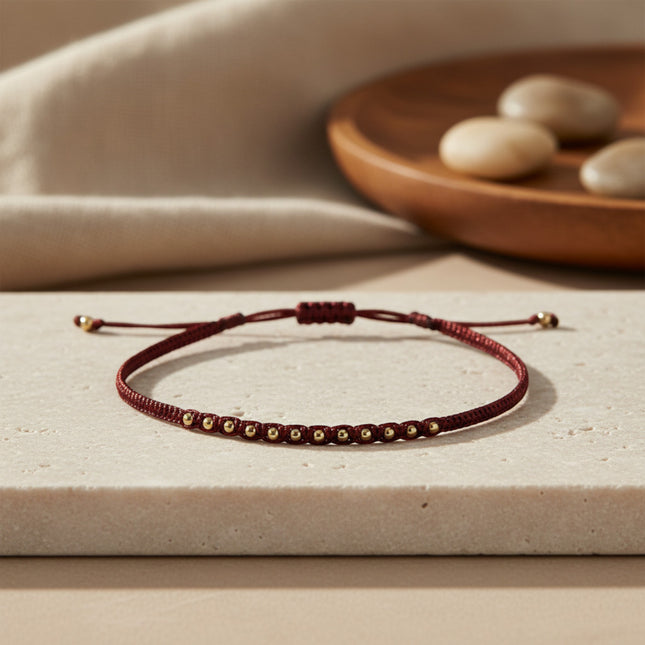 Bracelet fin LeJu en fil de polyester bordeaux avec billes en or rose, tissé main, ajustable.