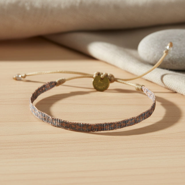 Bracelet fin tissé main horizons boutique en tons bronzés, ajustable, avec cordon ciré et médaille dorée.