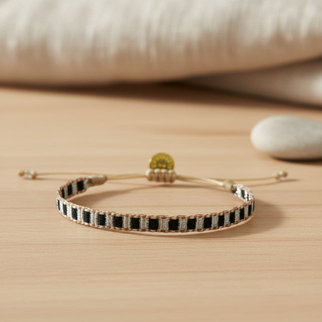 Bracelet tissé main Guanabana, 5mm de large, avec des motifs géométriques noirs et blancs sur fond beige, cordon ajustable et breloque dorée.