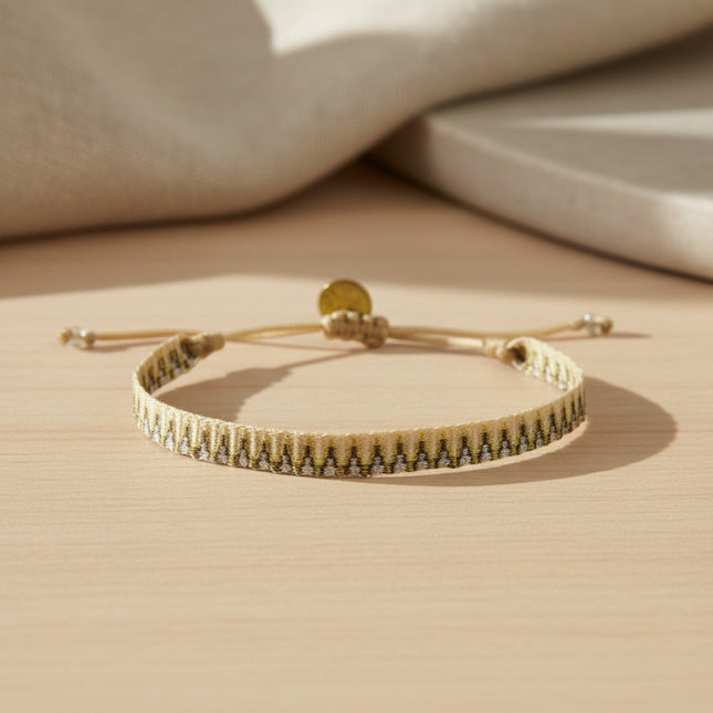 Bracelet tissé main horizons boutique en tons or, avec cordon ajustable et breloque dorée. Style ethnique et moderne.