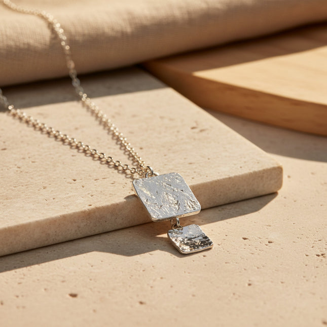 Collier Alcyone fin de horizons boutique en argent avec deux pendentifs carrés texturés superposés et une chaîne à maillons fins.