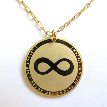 Collier horizons boutique en laiton plaqué or, médaille ronde gravée symbole infini et texte "L'ESPACE EST L'ORDRE DES CHOSES QUI COEXISTENT".
