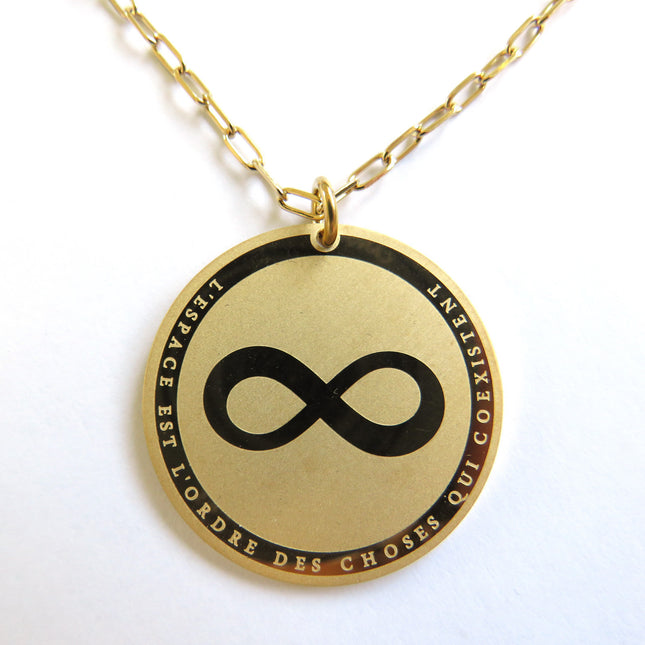 Collier horizons boutique en laiton plaqué or, médaille ronde gravée symbole infini et texte "L'ESPACE EST L'ORDRE DES CHOSES QUI COEXISTENT".